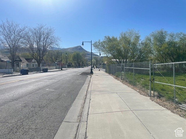 View of asphalt street with sidewalks, curbs, a mountain view, and street lights