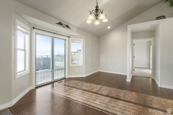 Spare room featuring a chandelier, dark wood-type flooring, lofted ceiling, and baseboards