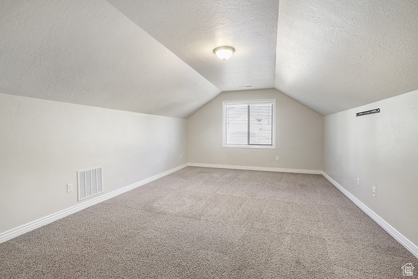 Bonus room featuring a textured ceiling, carpet, lofted ceiling, and baseboards