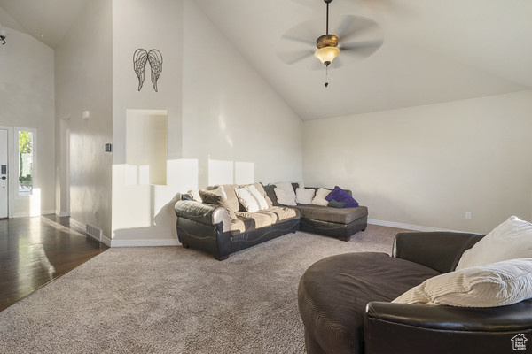 Carpeted living room featuring high vaulted ceiling, baseboards, and ceiling fan