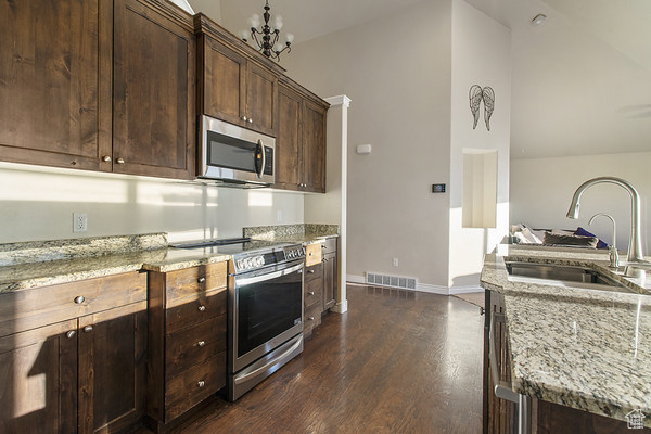 Kitchen with stainless steel appliances, a sink, light stone countertops, dark wood finished floors, and vaulted ceiling