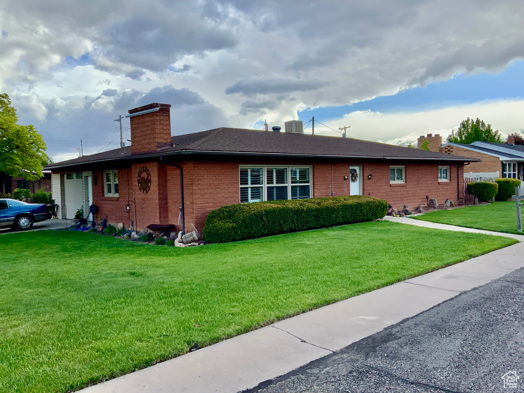 Ranch-style house featuring a chimney, a garage, brick siding, a front yard, and central air condition unit