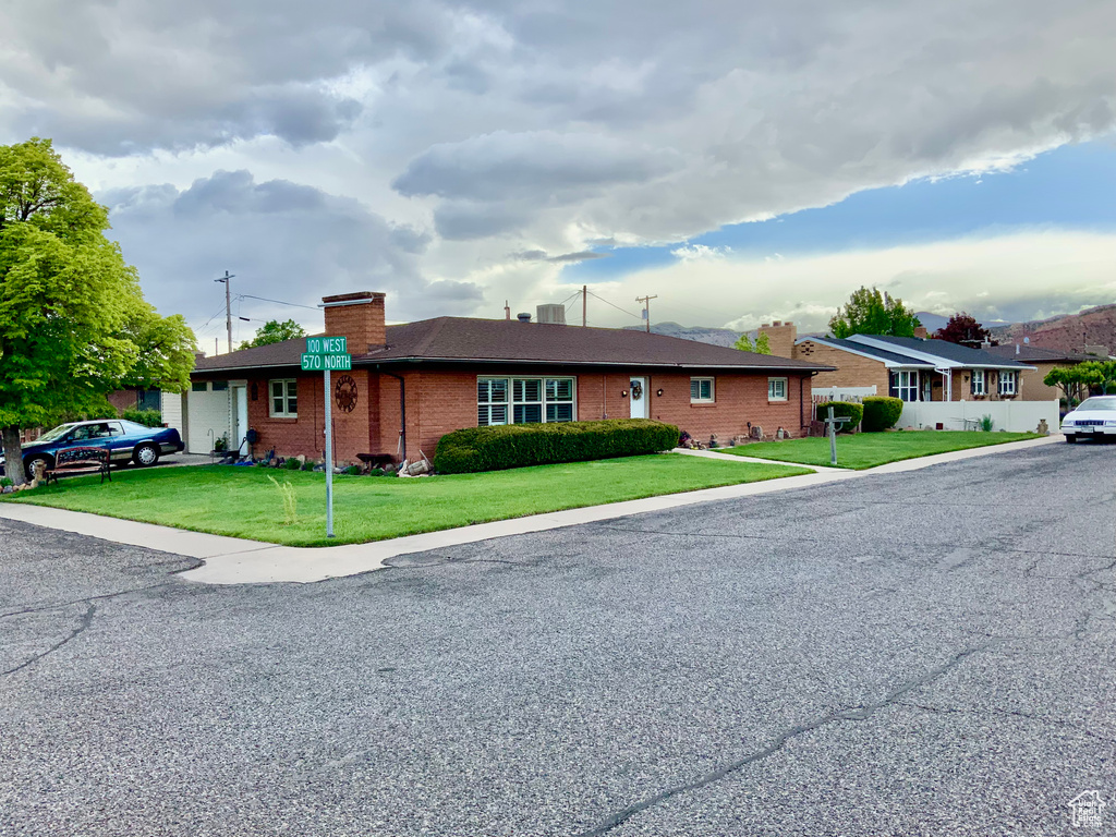 Ranch-style house featuring a chimney, a garage, brick siding, and a front lawn