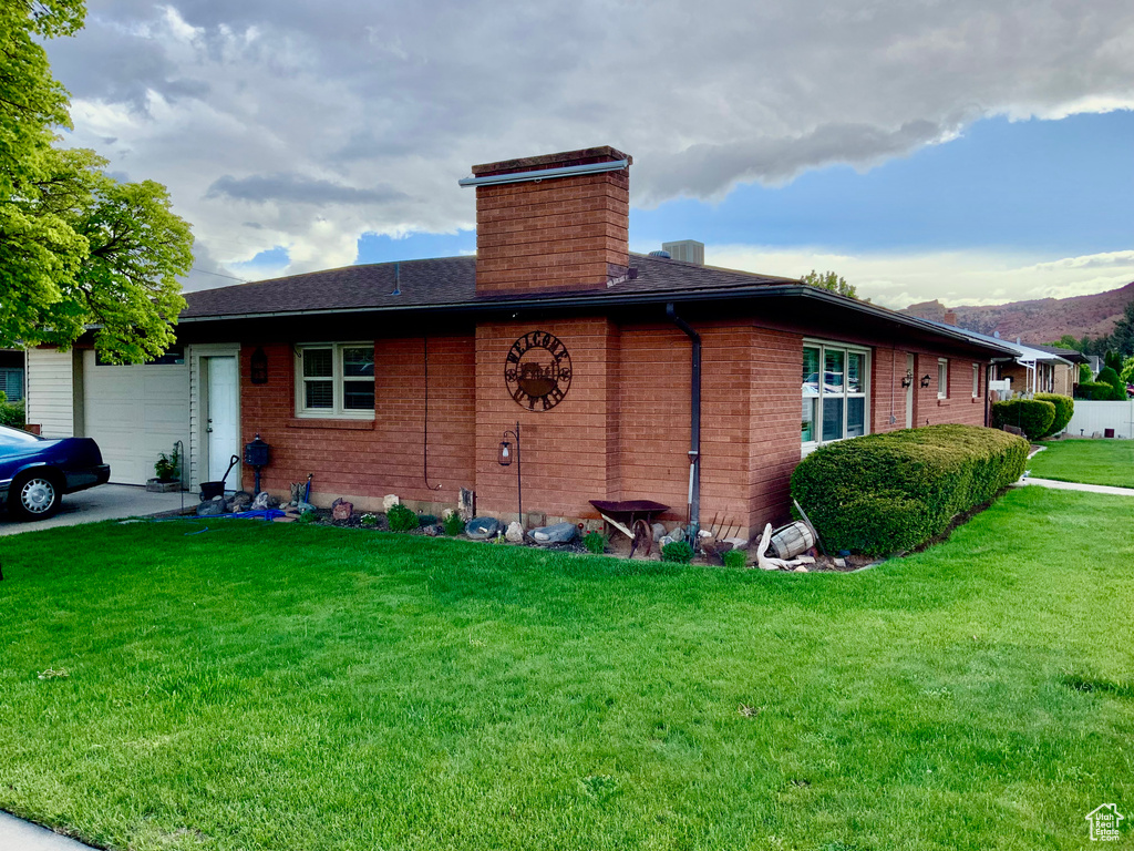 View of property exterior with a chimney, a garage, a yard, a mountain view, and brick siding