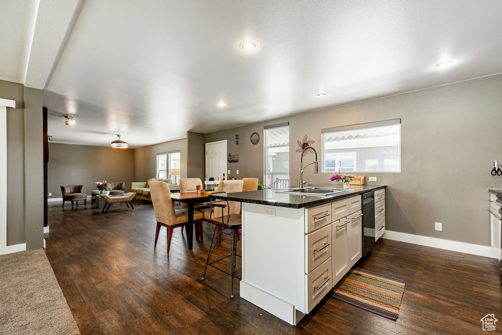 Kitchen featuring a peninsula, a sink, open floor plan, dishwashing machine, and a kitchen breakfast bar