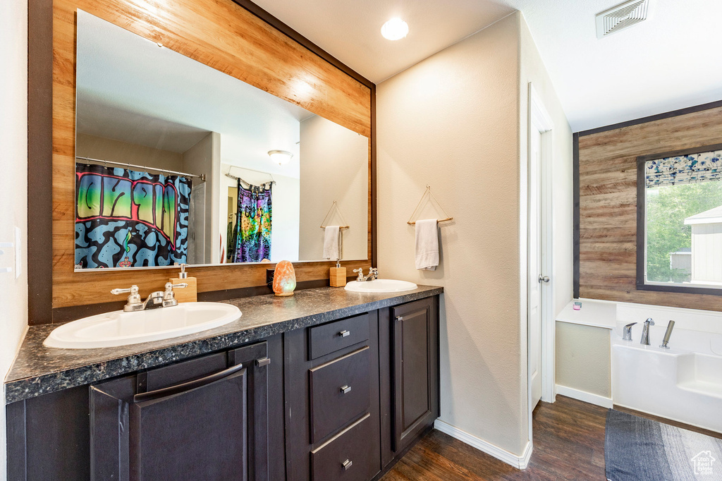 Bathroom with wood finished floors, baseboards, a bath, and double vanity