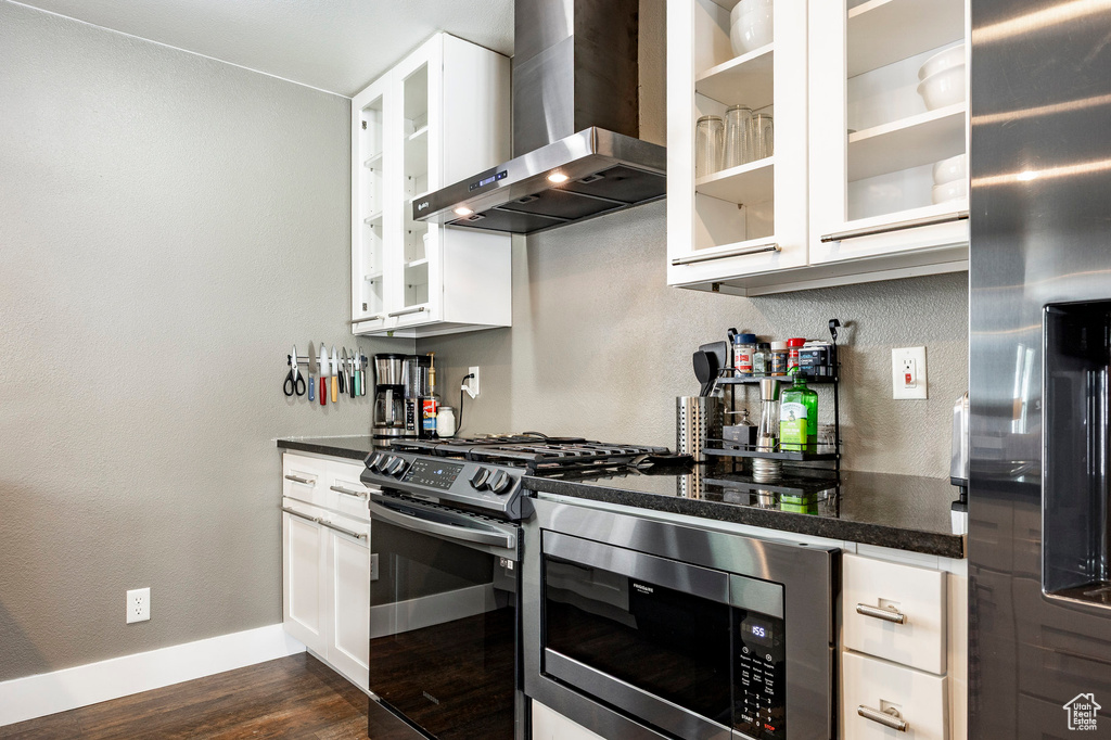 Kitchen featuring wall chimney exhaust hood, stainless steel appliances, dark wood-type flooring, white cabinets, and a textured wall