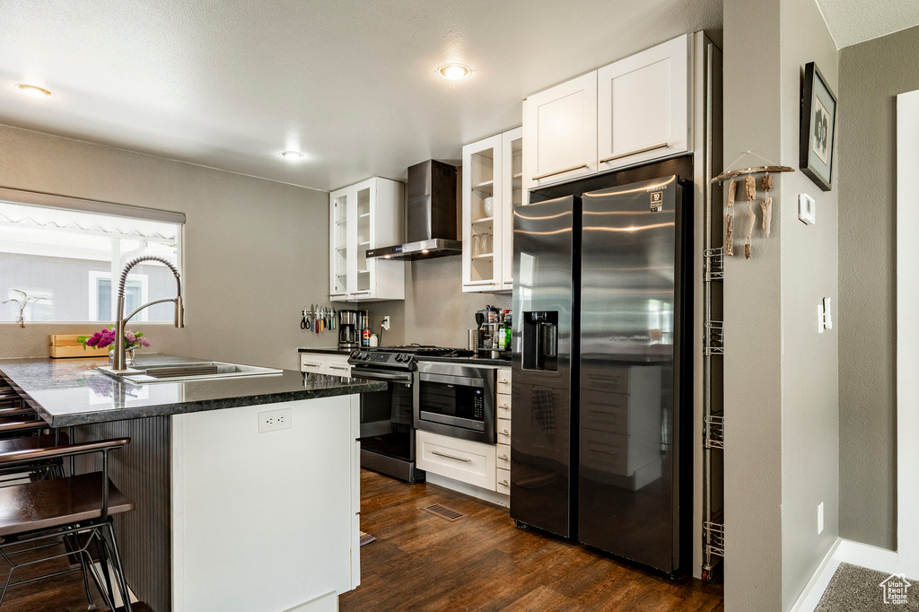 Kitchen with stainless steel appliances, wall chimney range hood, a sink, a breakfast bar, and glass insert cabinets