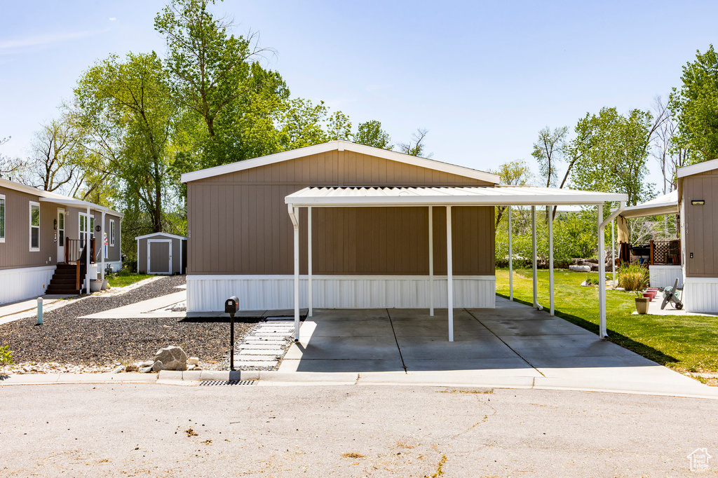 View of side of home with a storage unit, an outdoor structure, a carport, and a yard
