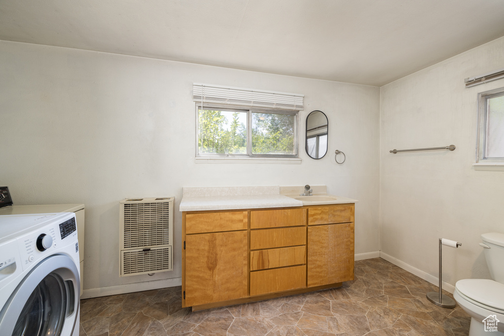 Bathroom featuring washer / dryer, heating unit, toilet, stone finish flooring, and baseboards