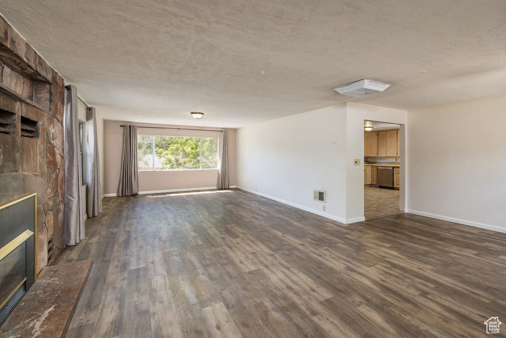 Unfurnished living room featuring a textured ceiling, dark wood-type flooring, baseboards, and a stone fireplace