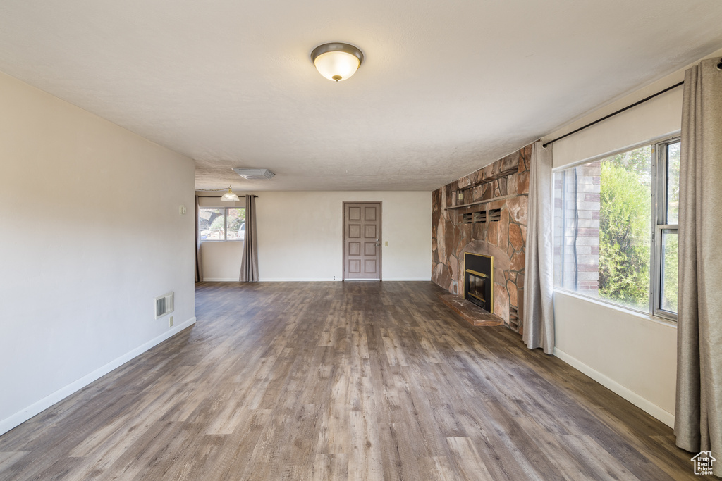 Unfurnished living room with wood finished floors, a stone fireplace, and baseboards