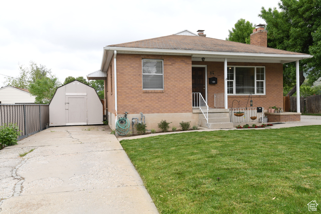 View of front of house featuring brick siding, a storage unit, a chimney, an outdoor structure, and a shingled roof
