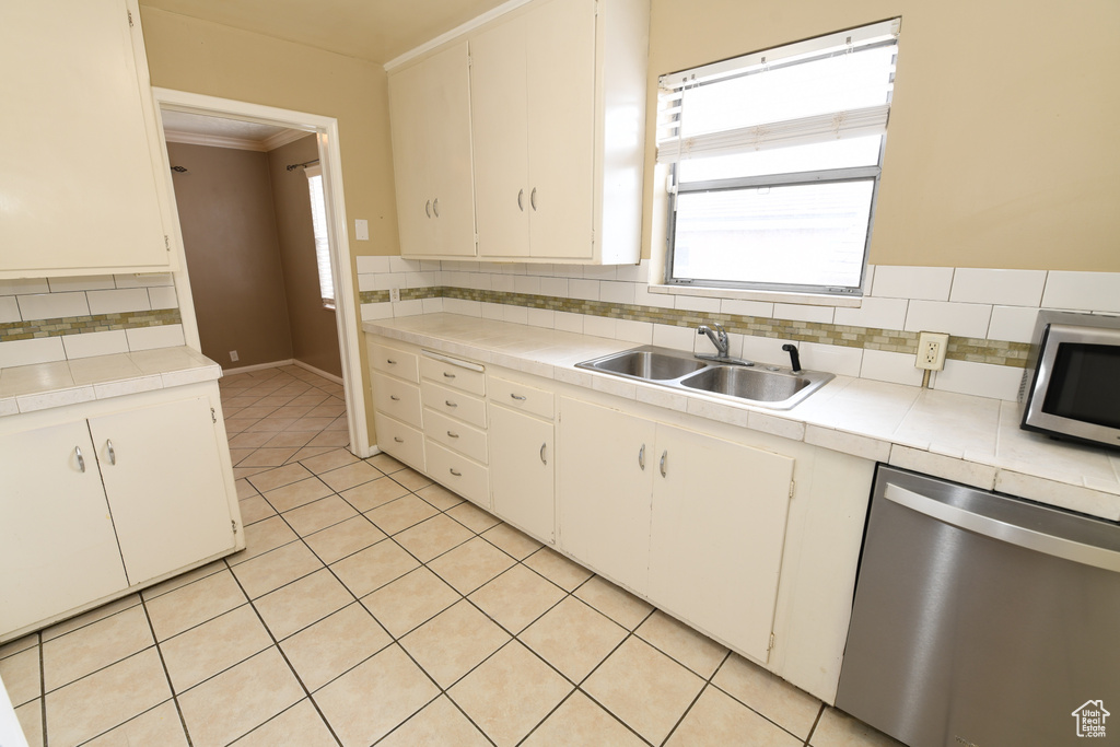 Kitchen with stainless steel appliances, tile countertops, a sink, tasteful backsplash, and ornamental molding