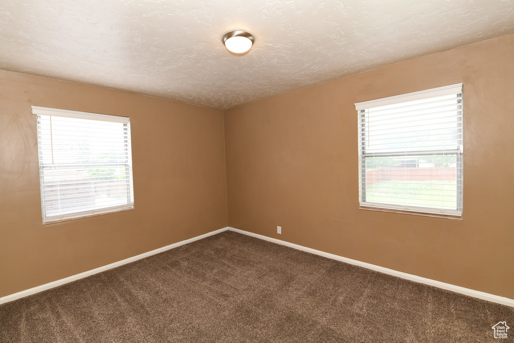 Empty room featuring dark carpet, baseboards, and a textured ceiling