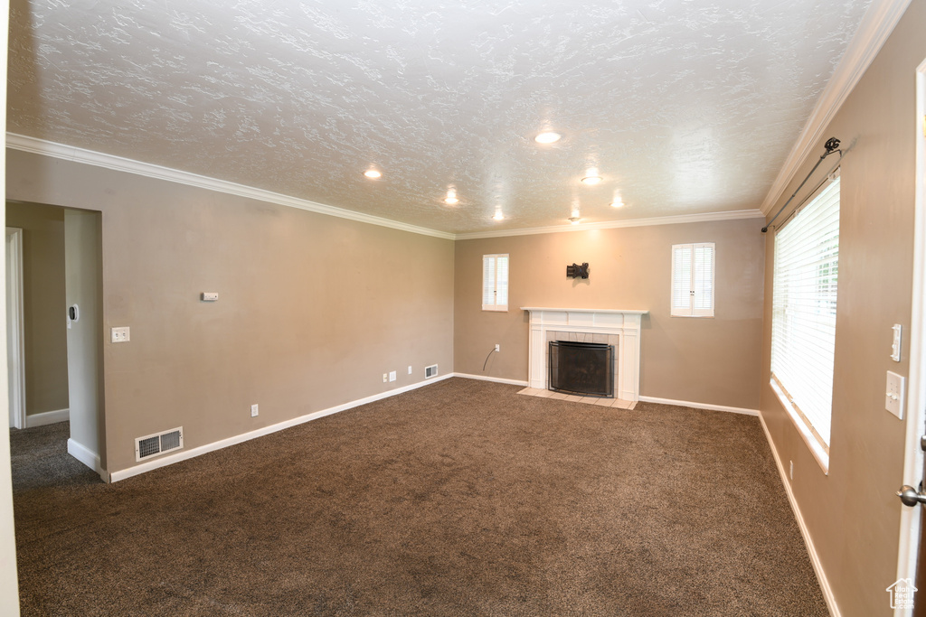 Unfurnished living room with a fireplace, dark colored carpet, baseboards, crown molding, and a textured ceiling
