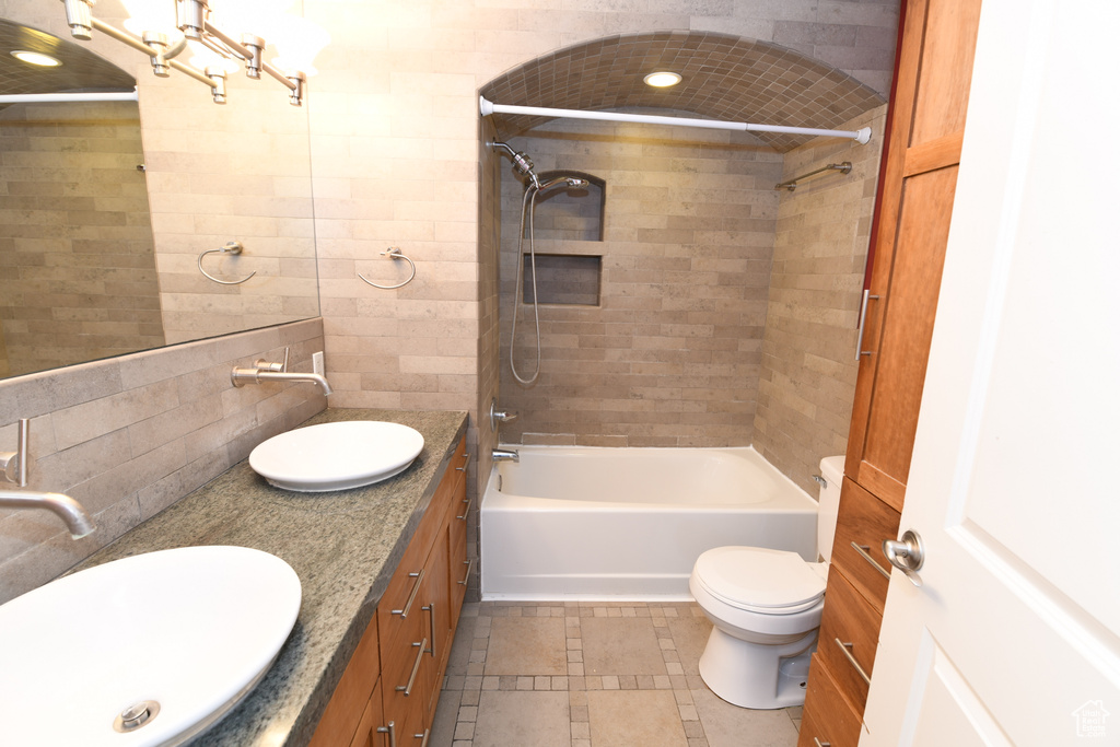 Bathroom with double vanity, shower / bath combination, tile walls, and toilet