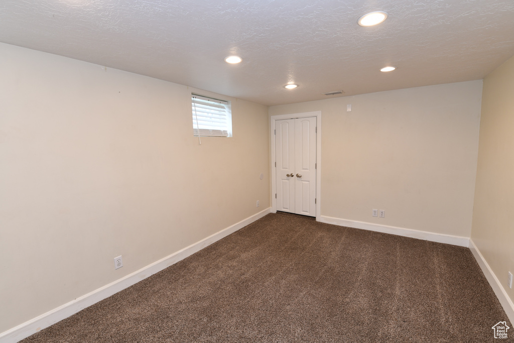 Below grade area featuring dark colored carpet, baseboards, recessed lighting, and a textured ceiling