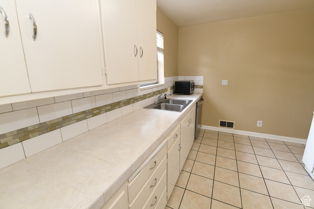 Kitchen featuring a sink, tile countertops, stainless steel dishwasher, white cabinets, and light tile patterned floors