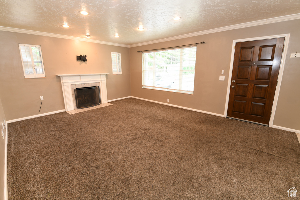 Unfurnished living room featuring baseboards, a fireplace, dark colored carpet, and crown molding