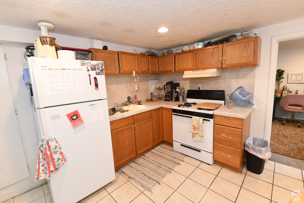 Kitchen with white appliances, under cabinet range hood, light countertops, decorative backsplash, and a textured ceiling