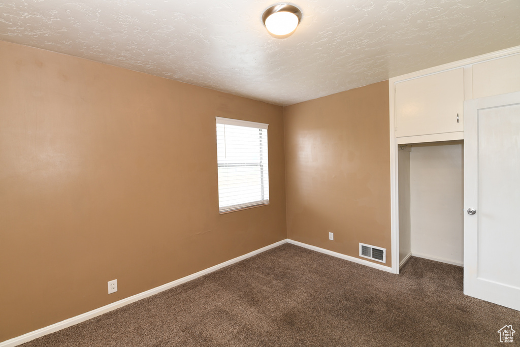 Unfurnished bedroom with dark colored carpet, baseboards, and a textured ceiling
