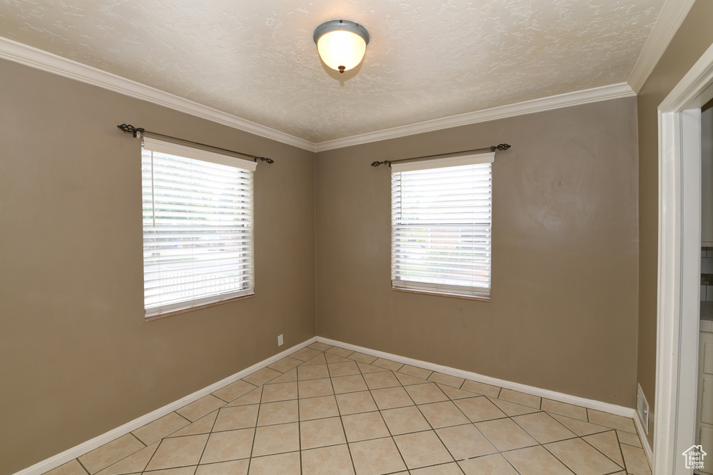 Unfurnished room with ornamental molding, light tile patterned floors, baseboards, and a textured ceiling
