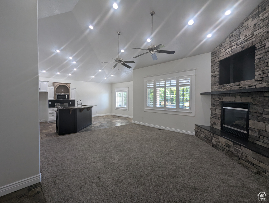 Unfurnished living room featuring vaulted ceiling, carpet floors, a stone fireplace, and a ceiling fan