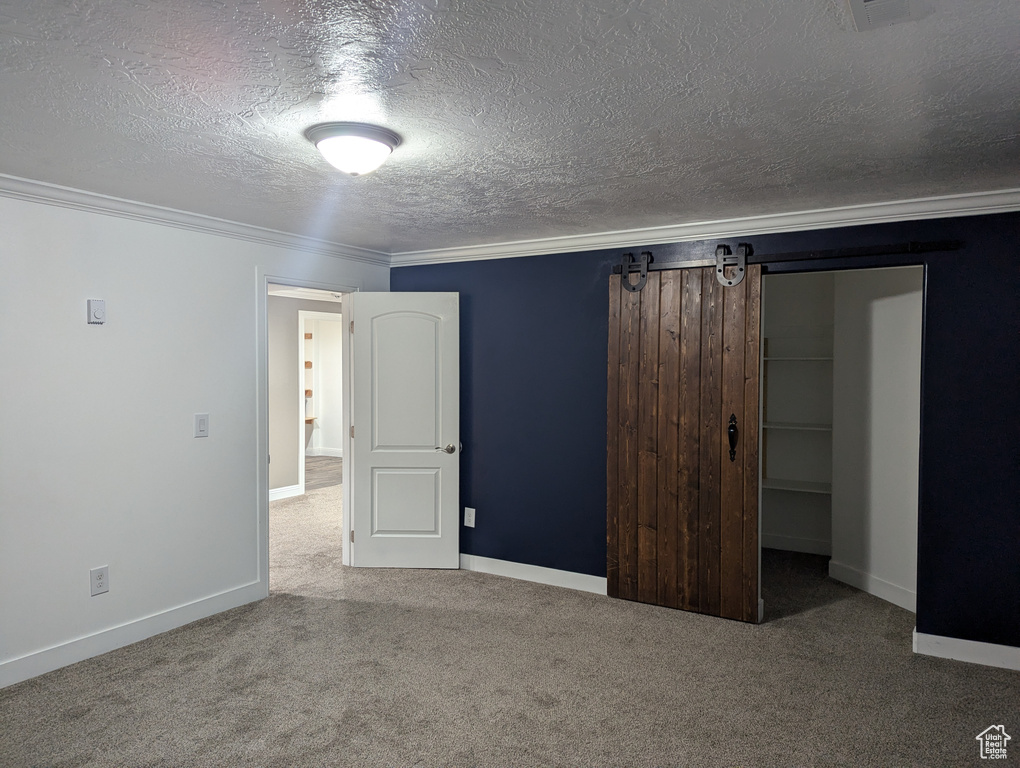 Unfurnished bedroom featuring carpet flooring, a textured ceiling, crown molding, a closet, and baseboards