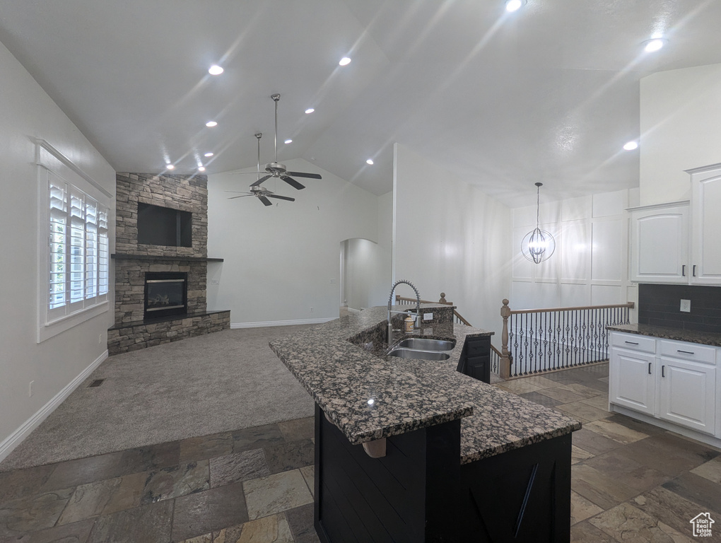 Kitchen with a ceiling fan, lofted ceiling, stone tile floors, dark stone counters, and arched walkways
