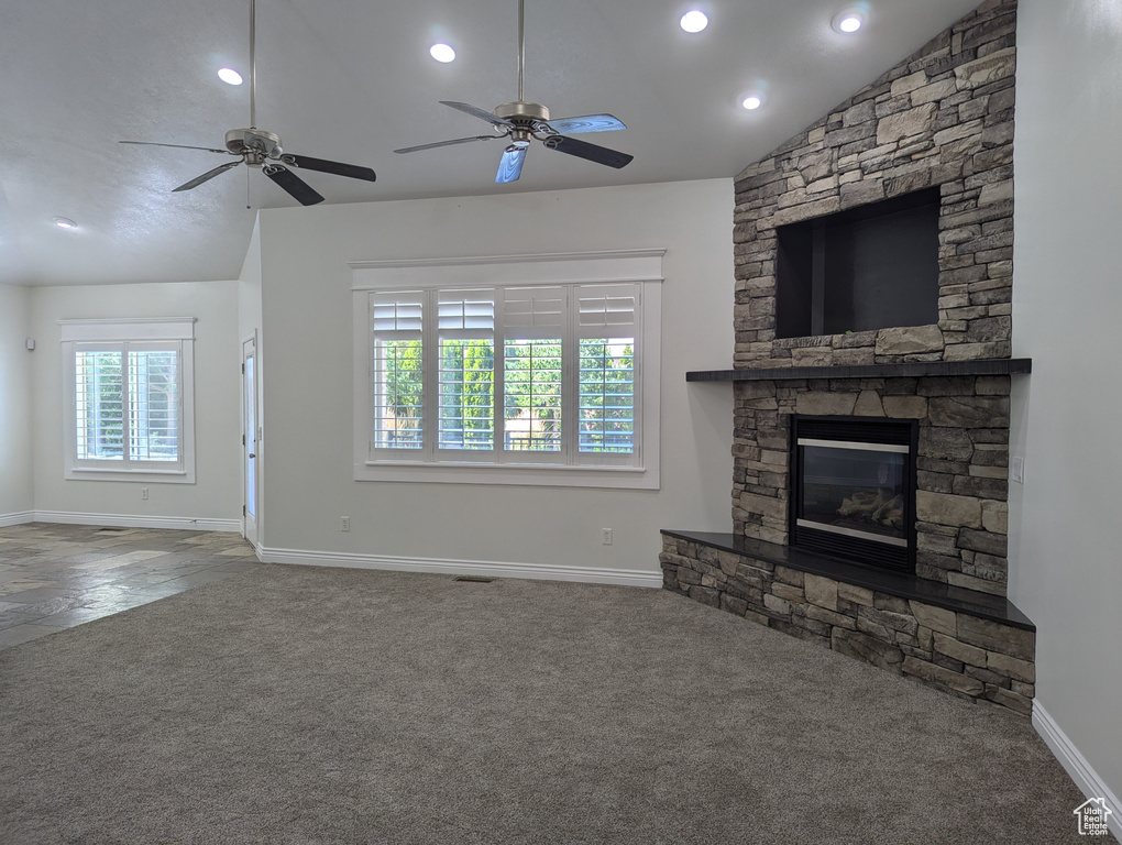 Unfurnished living room with carpet, vaulted ceiling, a stone fireplace, a ceiling fan, and recessed lighting