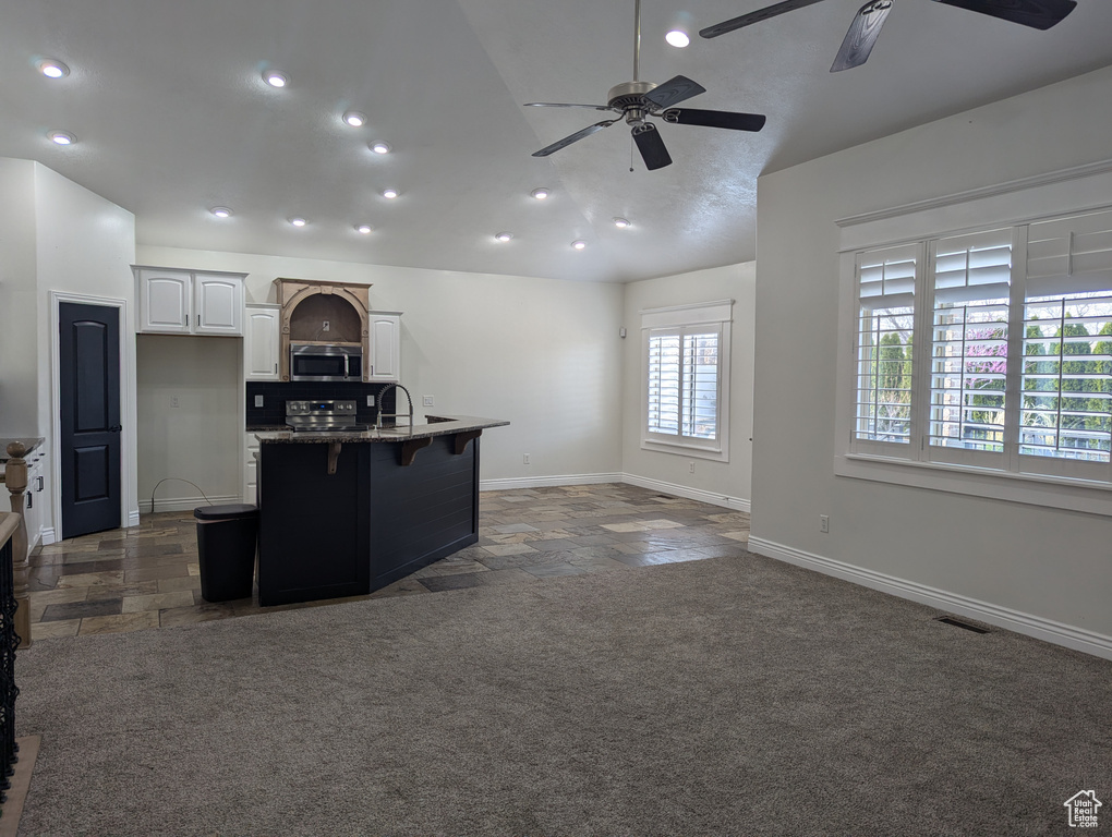 Kitchen with stainless steel appliances, ceiling fan, open floor plan, stone tile flooring, and lofted ceiling