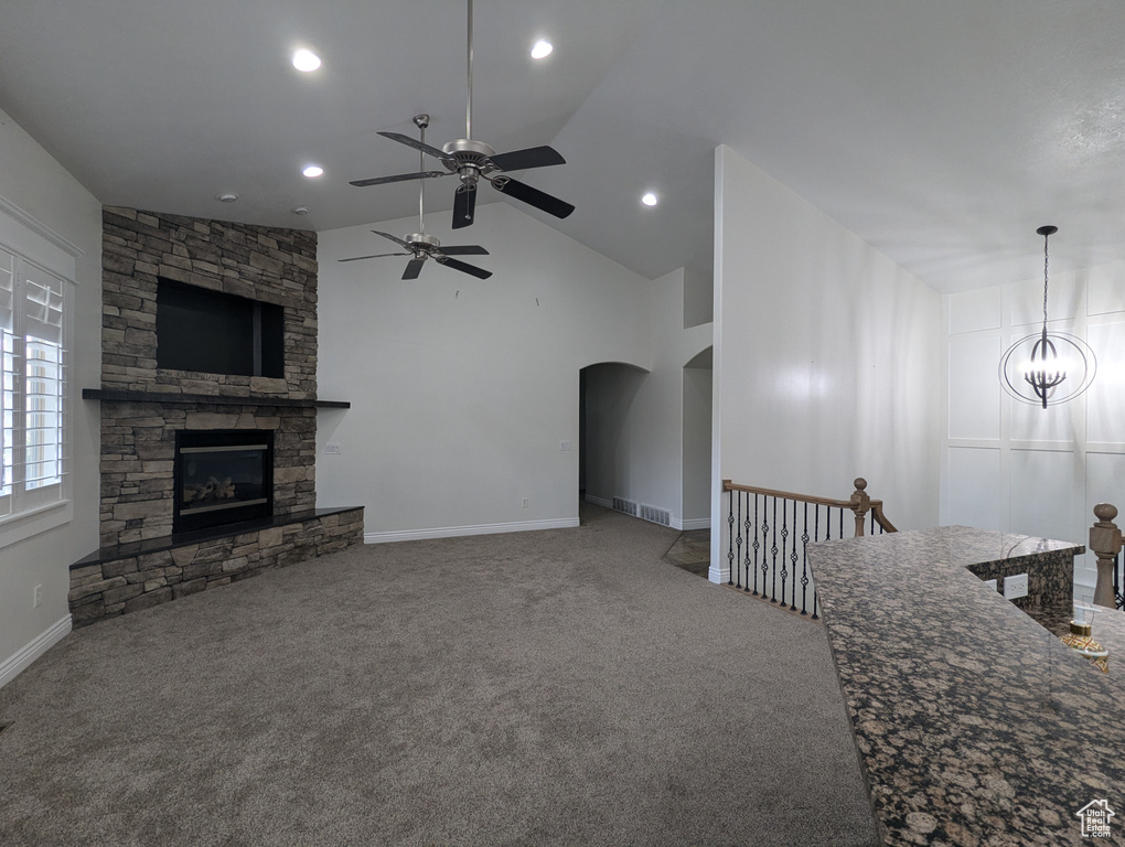 Unfurnished living room featuring carpet flooring, arched walkways, a ceiling fan, a fireplace, and vaulted ceiling