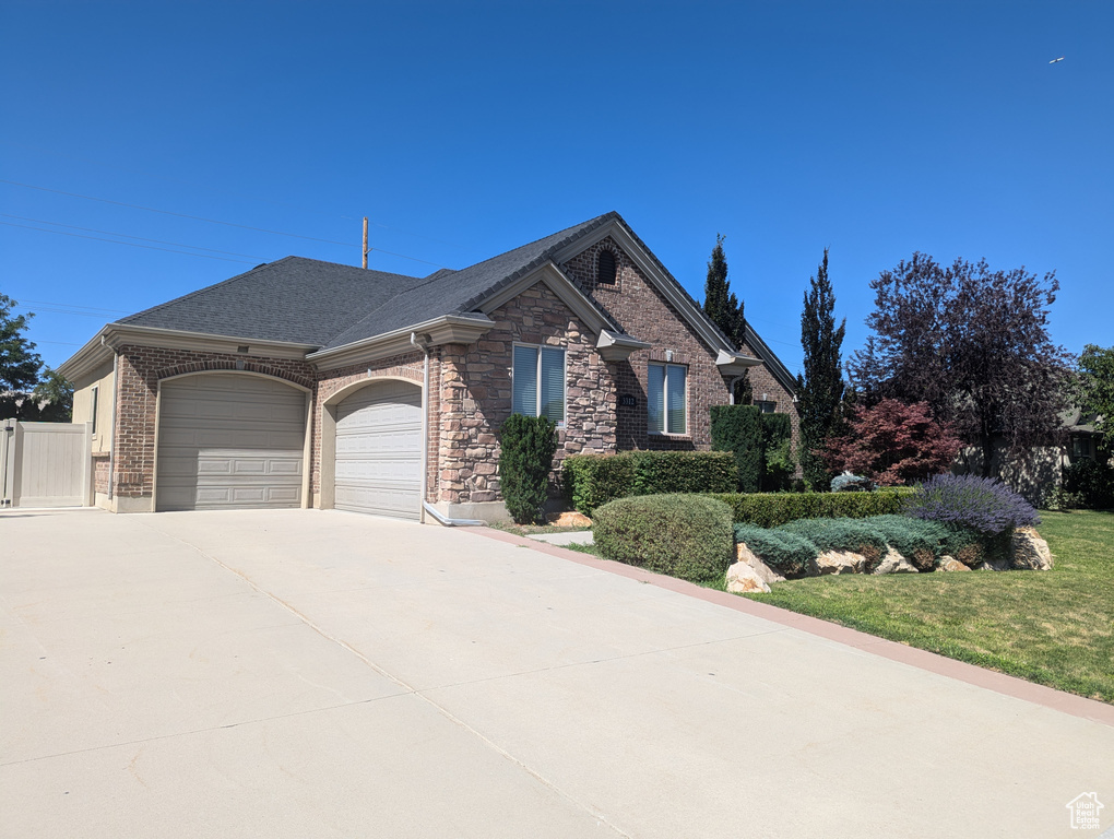 View of front of home featuring an attached garage, driveway, brick siding, a shingled roof, and stone siding