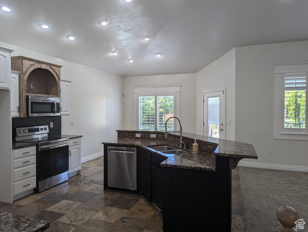 Kitchen featuring appliances with stainless steel finishes, recessed lighting, a kitchen breakfast bar, stone tile floors, and dark stone counters