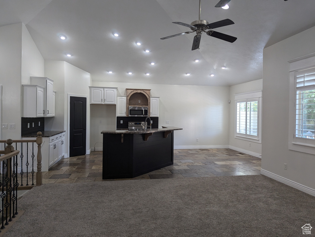 Kitchen featuring stainless steel microwave, stone tile floors, ceiling fan, white cabinetry, and high vaulted ceiling