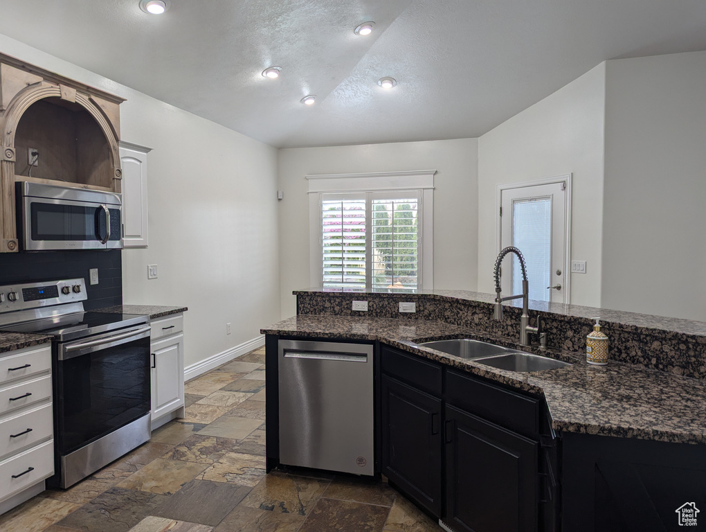Kitchen featuring appliances with stainless steel finishes, a sink, stone tile flooring, dark stone countertops, and a textured ceiling