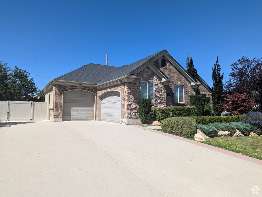 View of front of house with an attached garage, a gate, concrete driveway, brick siding, and stone siding