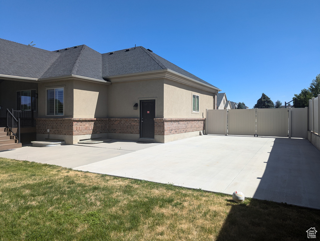 Back of house with brick siding, stucco siding, a gate, and a patio
