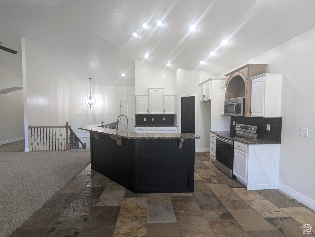 Kitchen with appliances with stainless steel finishes, tasteful backsplash, white cabinetry, dark stone countertops, and stone tile flooring