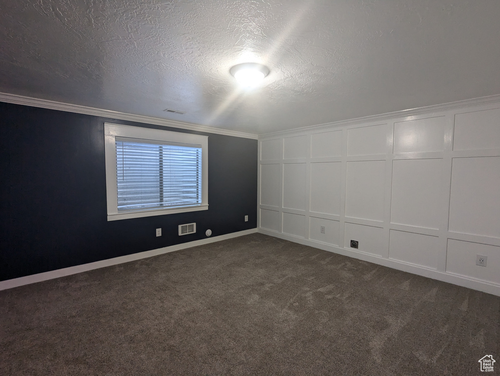 Spare room featuring a decorative wall, a textured ceiling, crown molding, and dark carpet