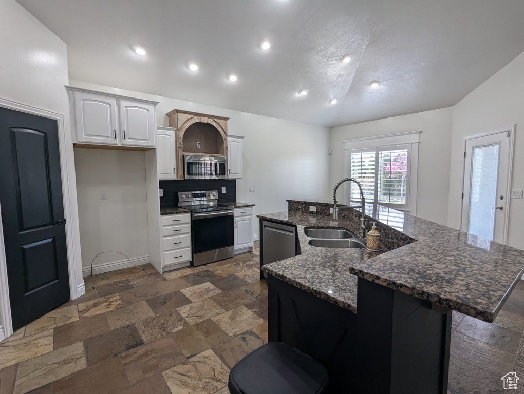 Kitchen with stainless steel appliances, a sink, vaulted ceiling, stone tile flooring, and a center island with sink