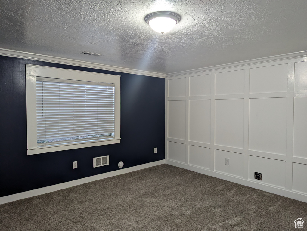 Empty room with a decorative wall, dark carpet, a textured ceiling, and baseboards
