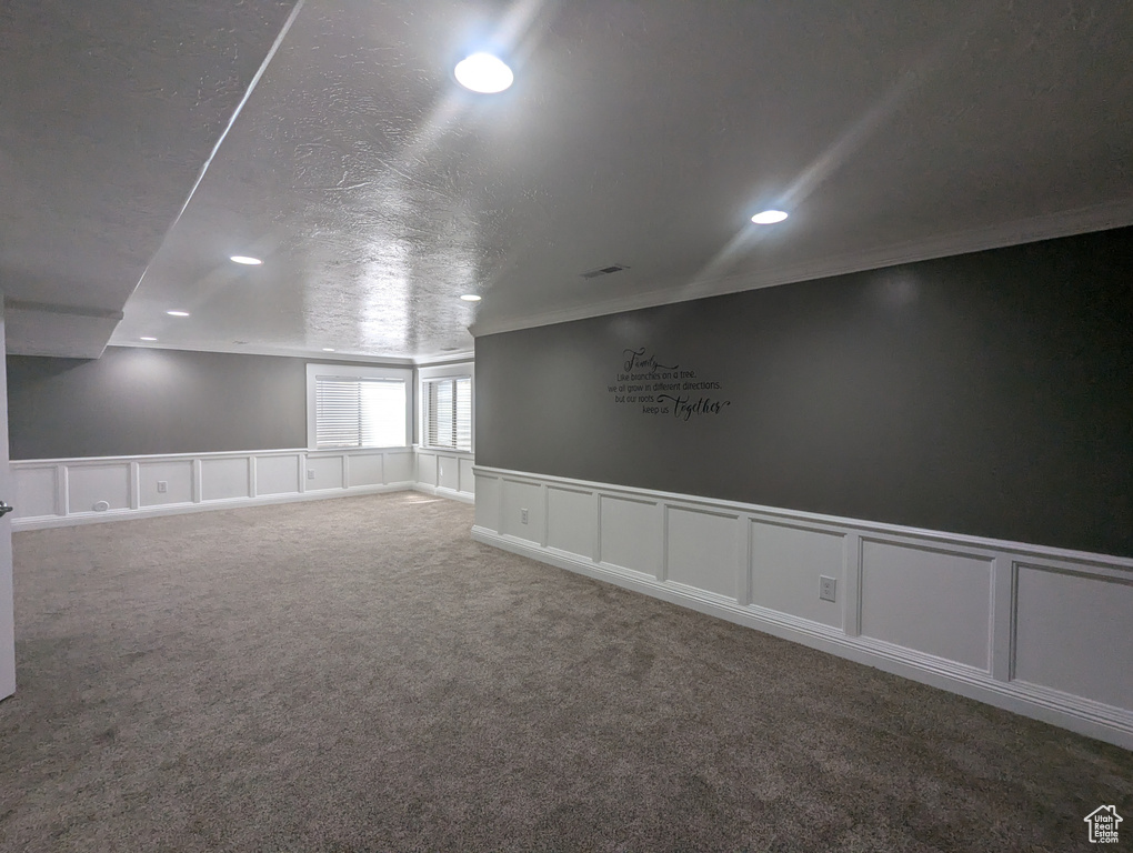 Carpeted empty room featuring a decorative wall, recessed lighting, ornamental molding, and a wainscoted wall