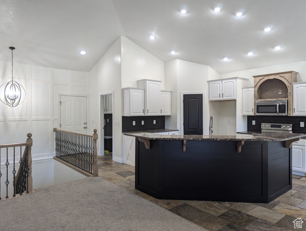 Kitchen featuring stainless steel appliances, lofted ceiling, backsplash, a breakfast bar area, and dark stone counters