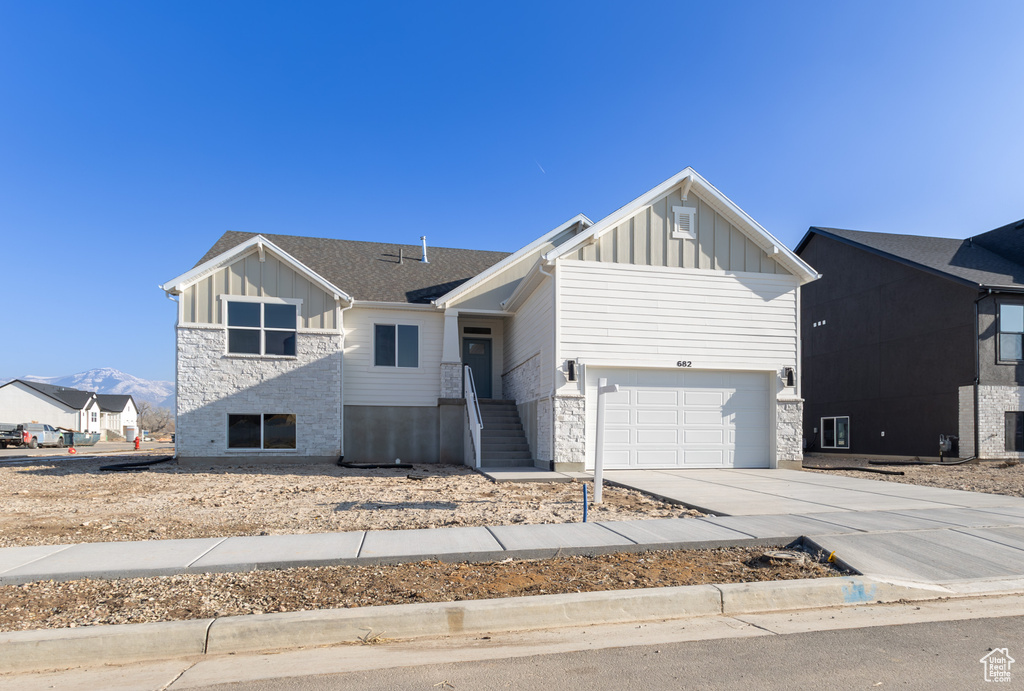 View of front of property featuring board and batten siding, driveway, stone siding, and a garage