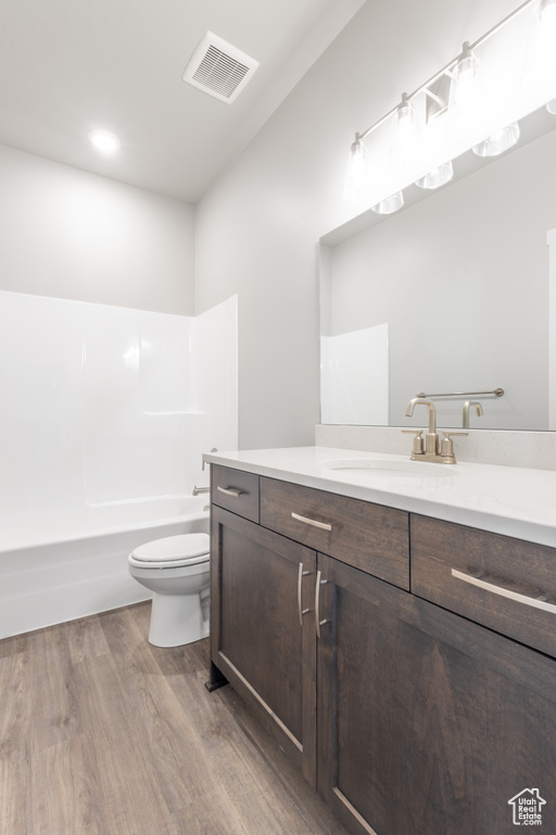 Bathroom with wood finished floors, toilet, vanity, washtub / shower combination, and recessed lighting