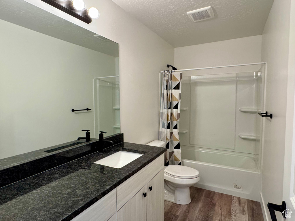 Bathroom featuring wood finished floors, toilet, a textured ceiling, vanity, and shower / bath combo with shower curtain