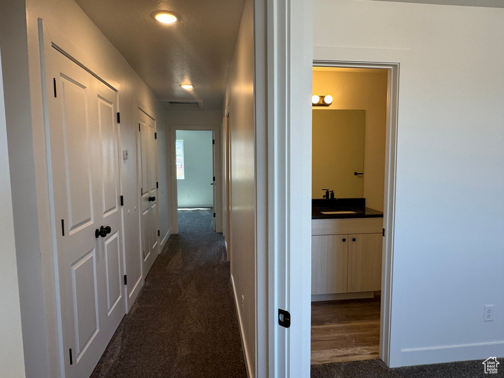Corridor with a sink, baseboards, dark carpet, and recessed lighting
