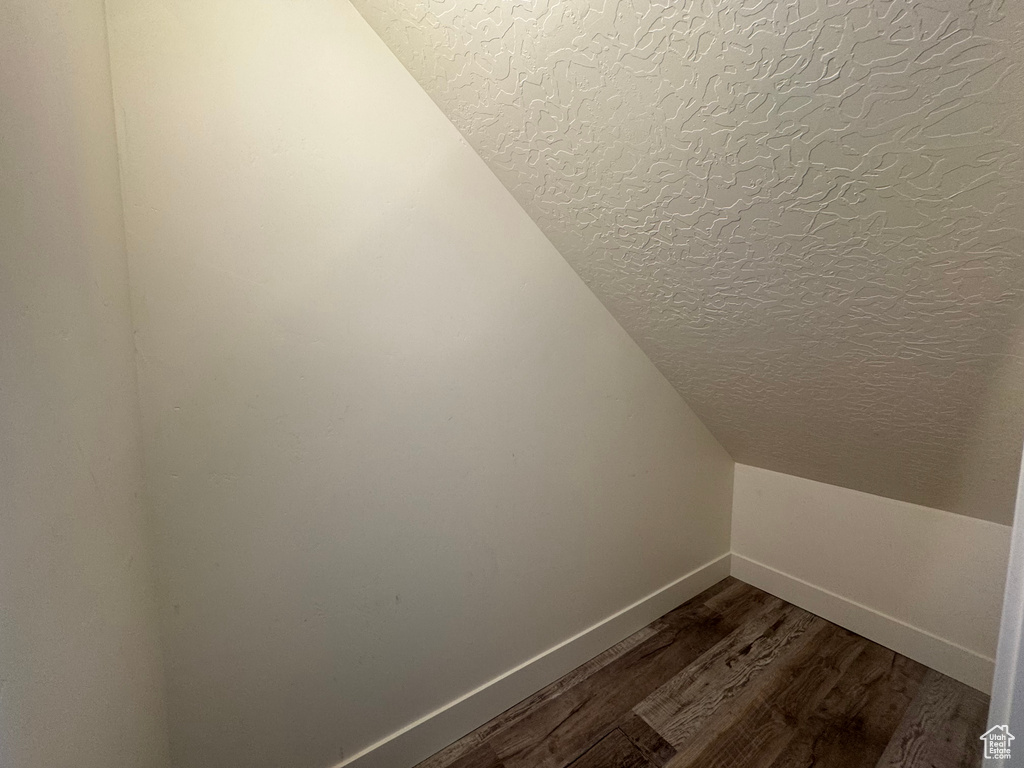 Bonus room with a textured ceiling, vaulted ceiling, baseboards, and dark wood-style flooring